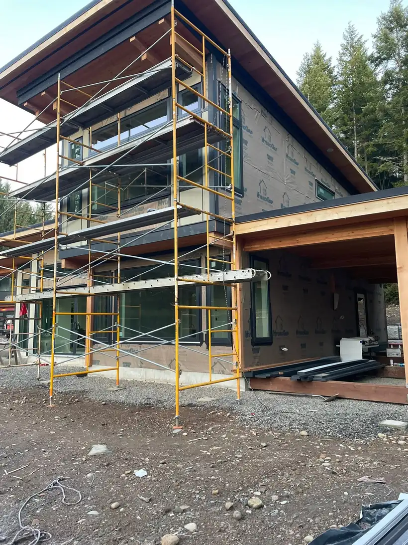 Custom home under construction with scaffolding, weather barrier, windows set, and a cedar-framed covered patio, by CKS Builders LLC in Clallam County, WA