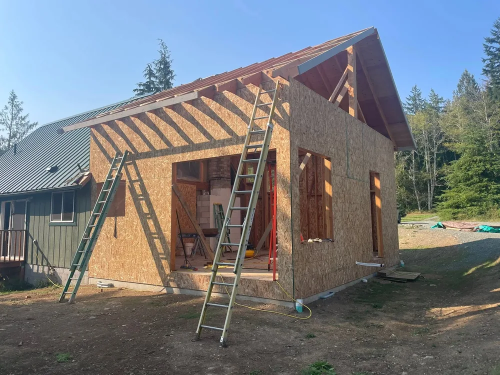 Framed and sheathed cottage with new rafters and a metal roof, ladders still in place, by CKS Builders LLC in Port Angeles, WA
