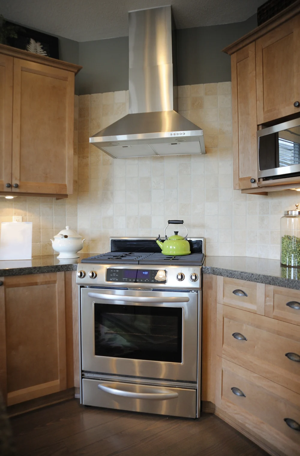 A tile backsplash covering the wall behind a kitchen range and a stainless vent hood