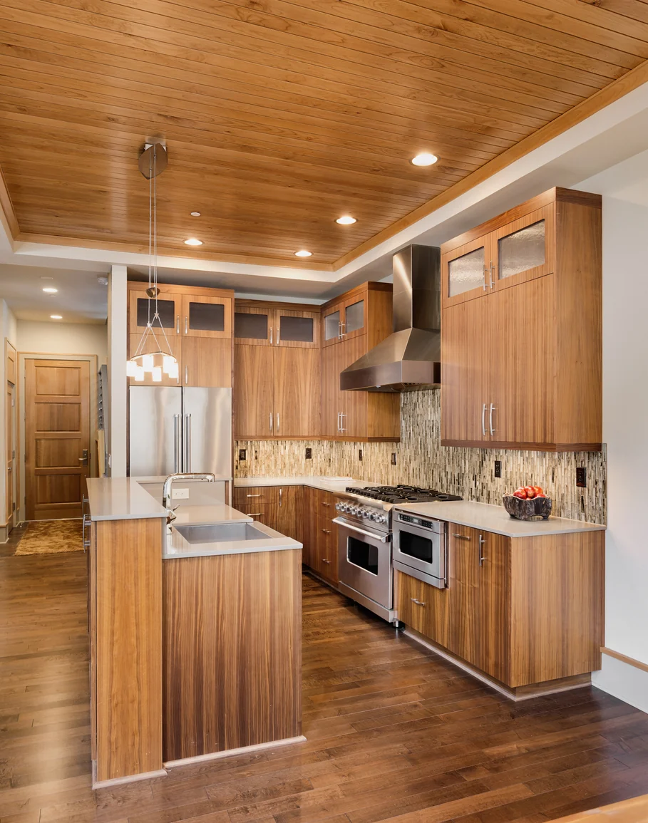 Kitchen with full-height wood cabinetry, a tile backsplash, a stainless range and hood, and a peninsula with a sink