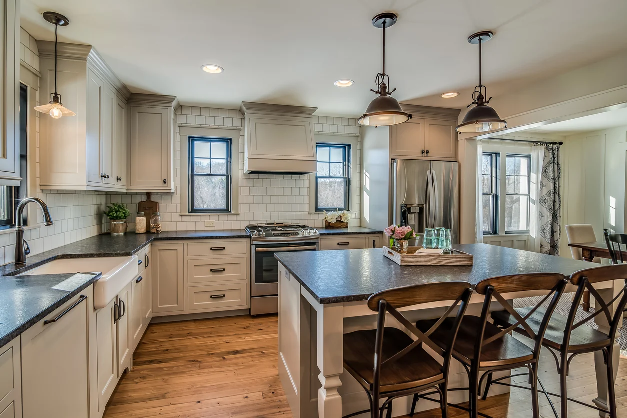 Hardwood flooring running through a kitchen with painted cabinetry and dark stone counters