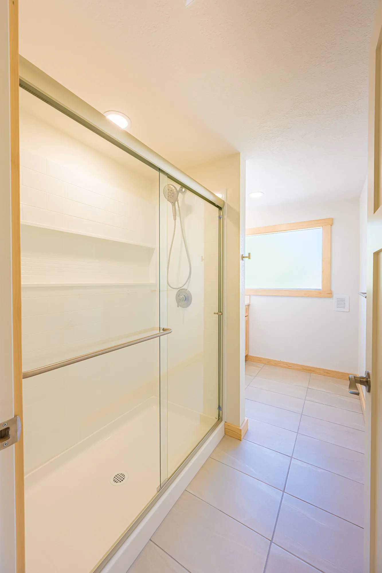 Remodeled bathroom with a glass-door shower, light tile flooring, and wood trim, by CKS Builders LLC