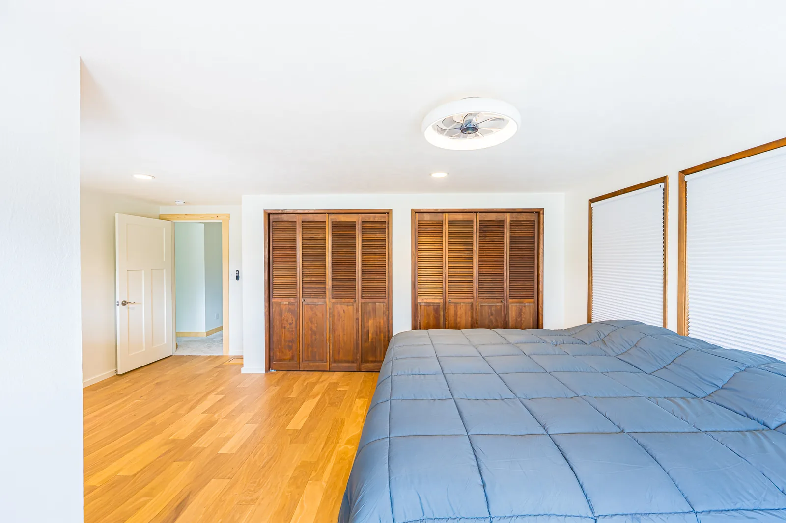 Bedroom with wood flooring, louvered wood closet doors, and a ceiling fan light in a home remodeled by CKS Builders LLC