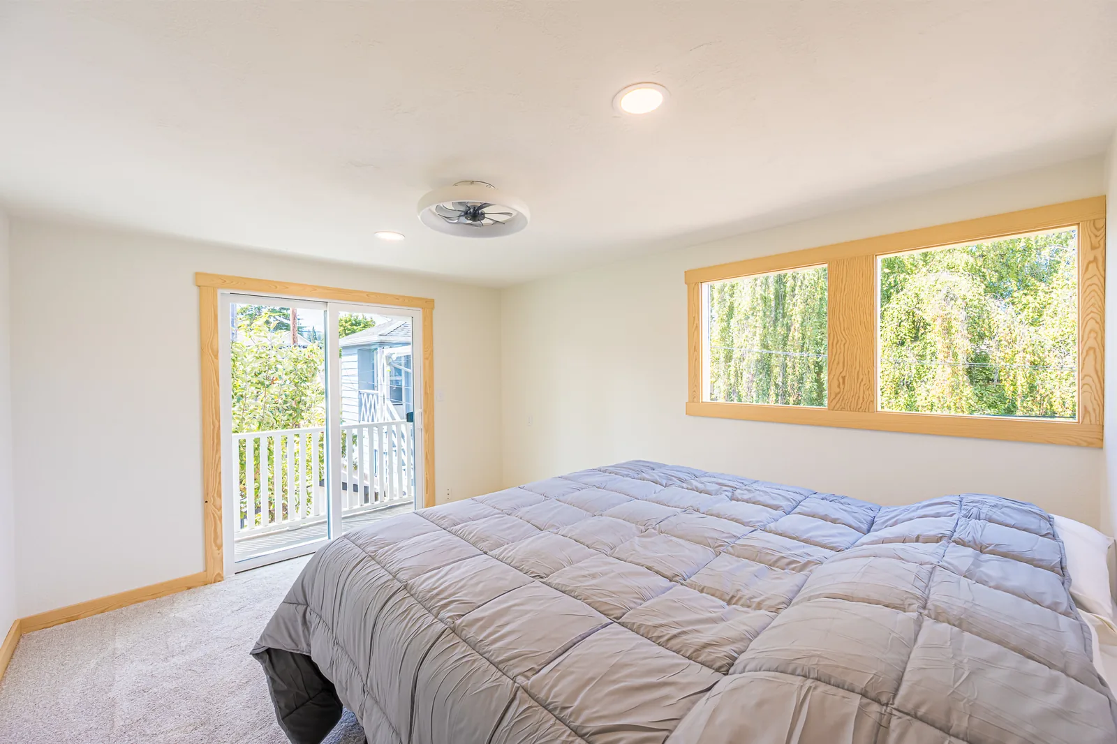 Carpeted bedroom with a glass door to a deck and wood-trimmed windows in a home remodeled by CKS Builders LLC