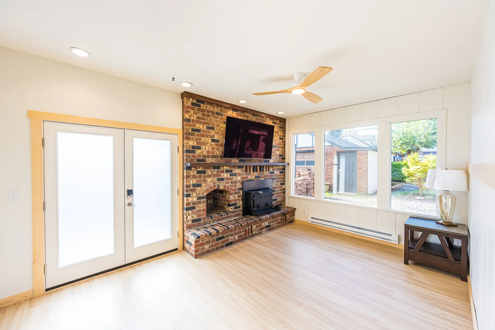 Family room with a brick fireplace and wood stove, French doors, and a wall of windows in a home remodeled by CKS Builders LLC
