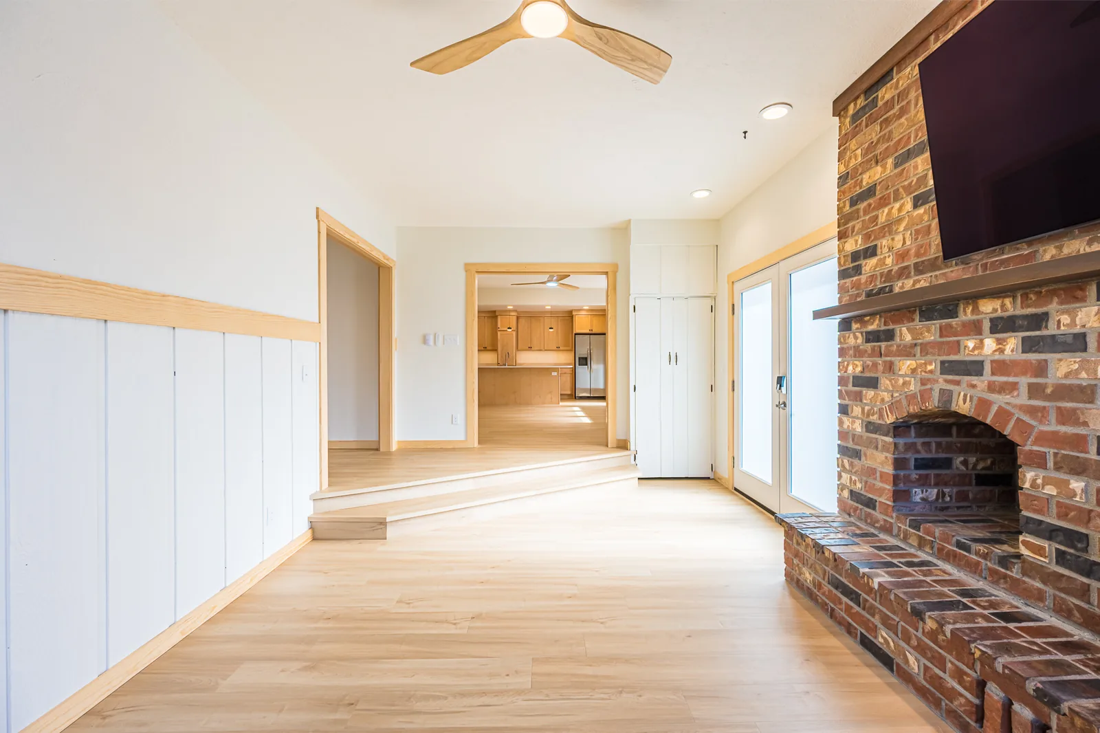 Family room with a brick fireplace, painted board wainscot, and a step up toward the kitchen in a home remodeled by CKS Builders LLC