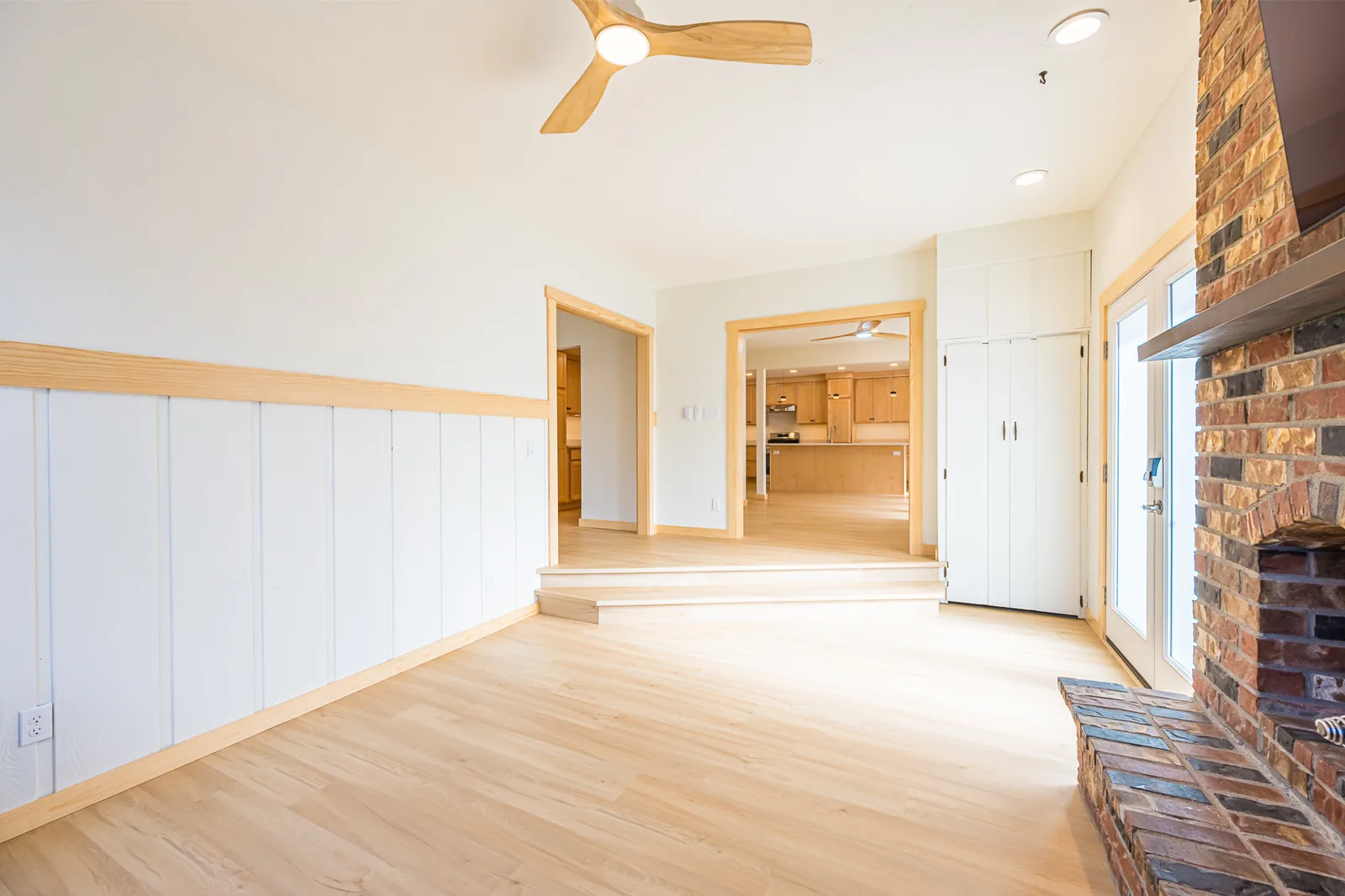 Family room with painted board wainscot and a brick fireplace, looking toward the kitchen, in a home remodeled by CKS Builders LLC