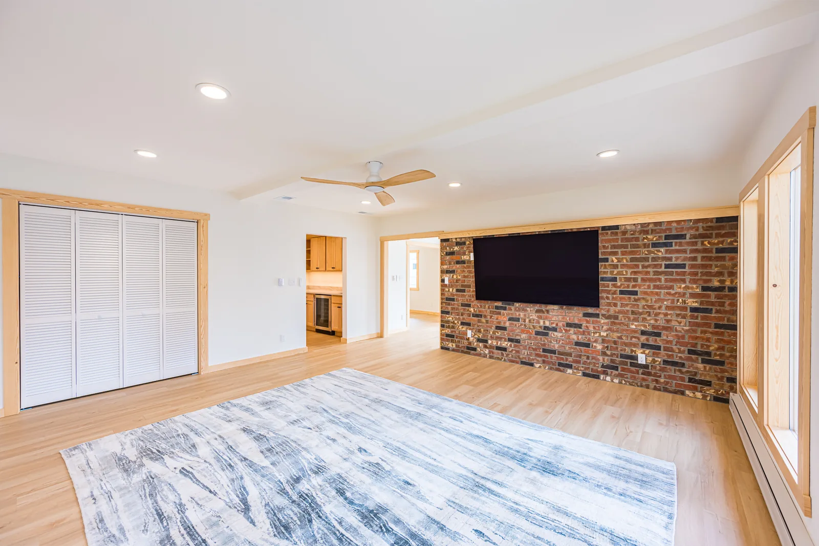 Living room with a brick feature wall, louvered closet doors, and light wood-look flooring in a home remodeled by CKS Builders LLC