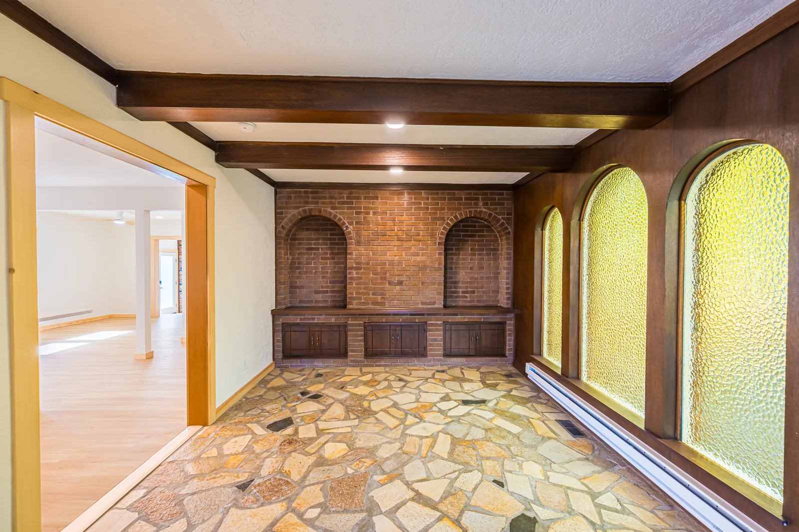 Room with dark ceiling beams, arched brick alcoves, arched textured-glass windows, and a flagstone floor in a home remodeled by CKS Builders LLC