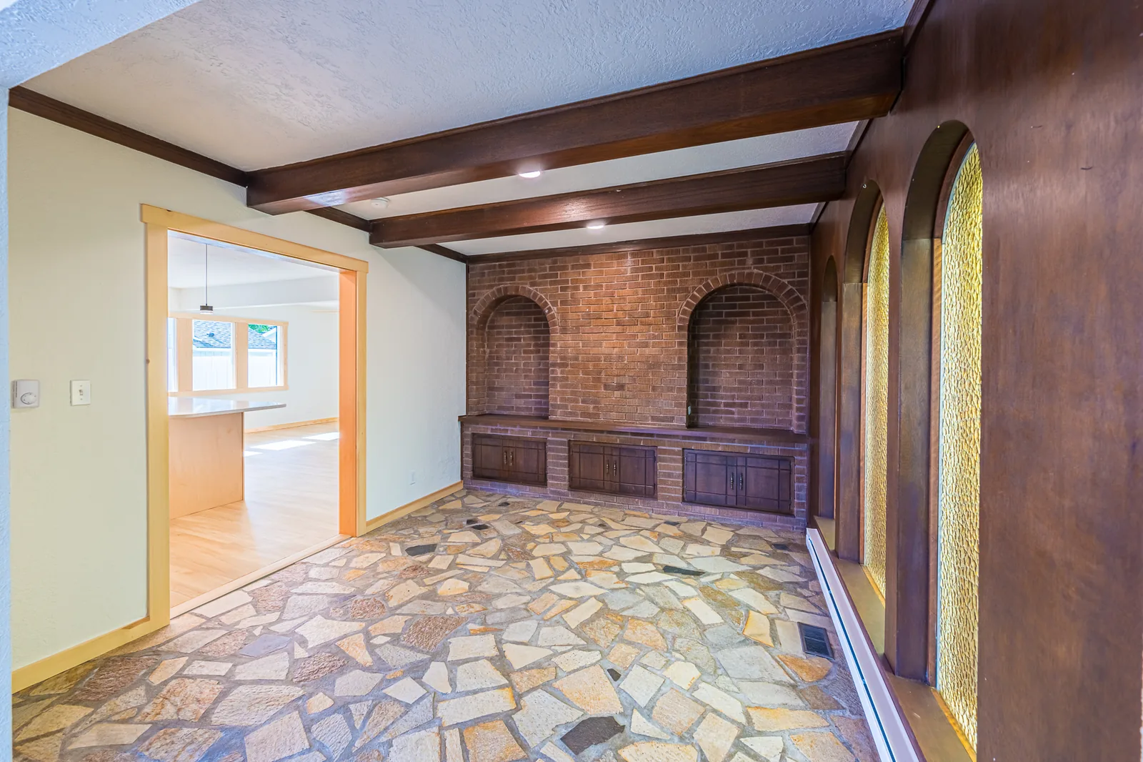 Flagstone-floored room with dark wood beams and arched brick alcoves, seen through a doorway, in a home remodeled by CKS Builders LLC