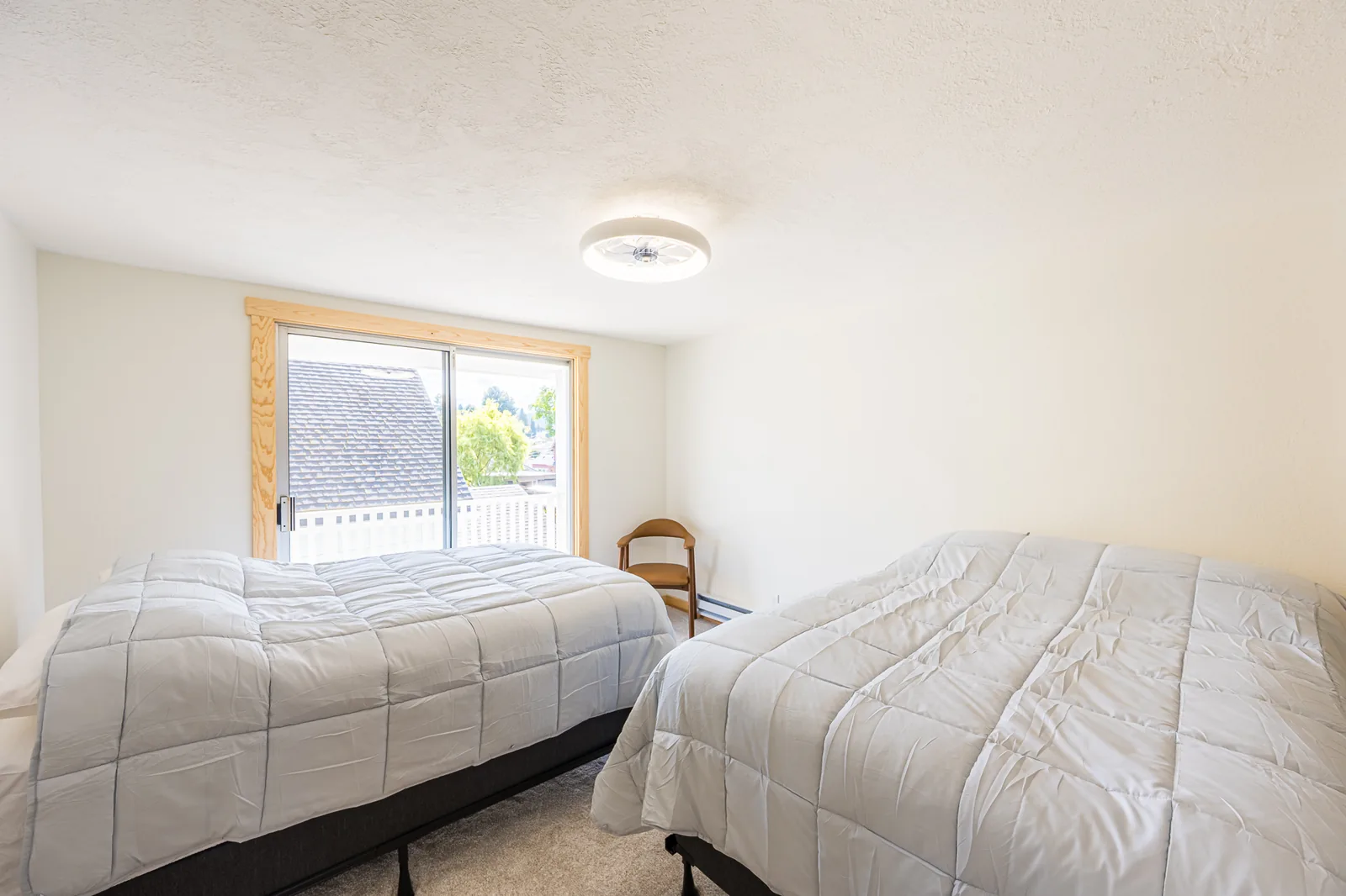 Carpeted bedroom with two beds and a sliding glass door in a home remodeled by CKS Builders LLC