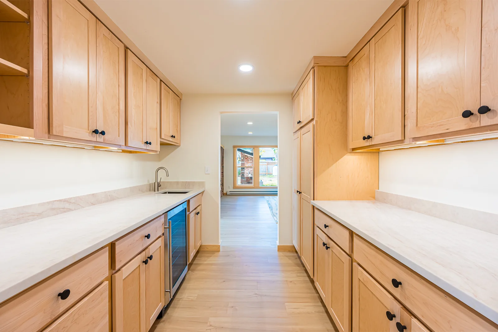 Galley kitchen with maple cabinets, a wine fridge, and light countertops, remodeled by CKS Builders LLC