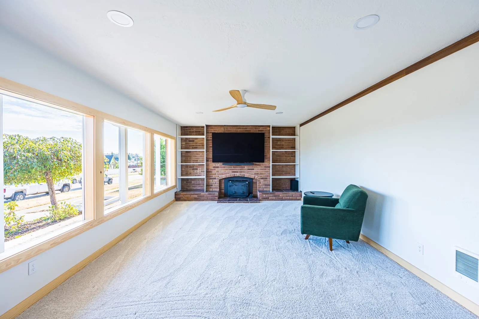 Carpeted living room with a brick fireplace, wood stove, built-in shelves, and a wall of windows, remodeled by CKS Builders LLC