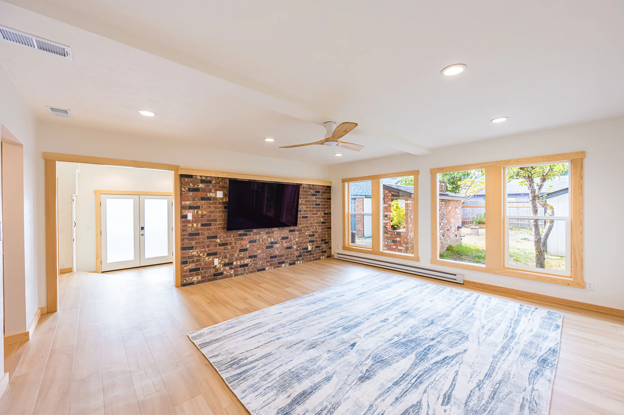 Remodeled living room with a brick feature wall, wood-trimmed windows, and light wood-look flooring, by CKS Builders LLC