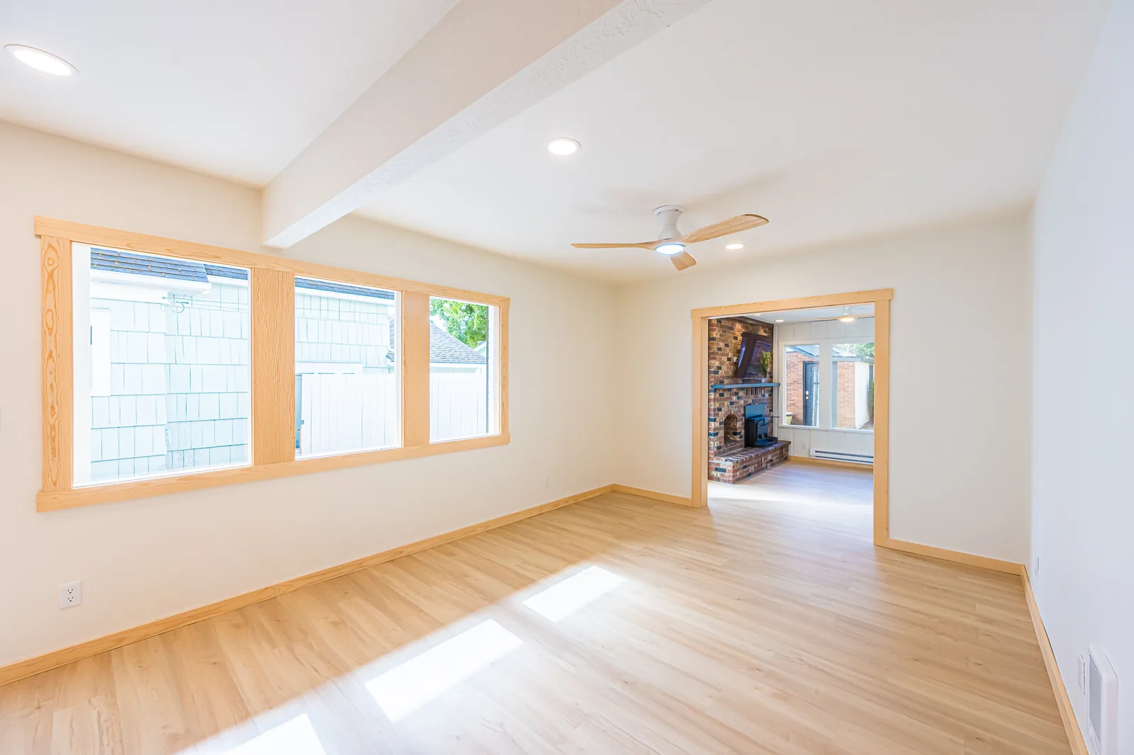 Open room with a painted ceiling beam, wood-trimmed windows, and light wood-look flooring in a home remodeled by CKS Builders LLC