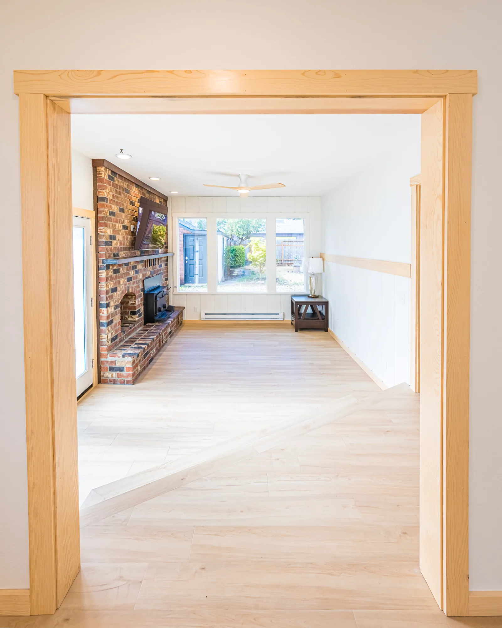 View through a wood-trimmed doorway into a family room with a brick fireplace, remodeled by CKS Builders LLC