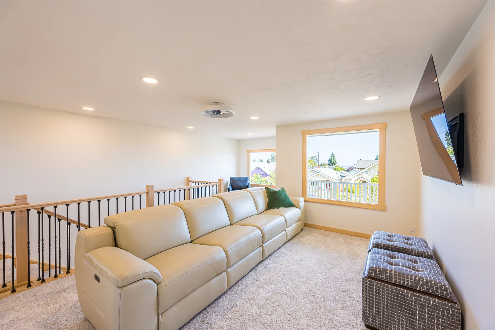 Upstairs sitting area with a sectional sofa behind a maple and black metal railing, remodeled by CKS Builders LLC