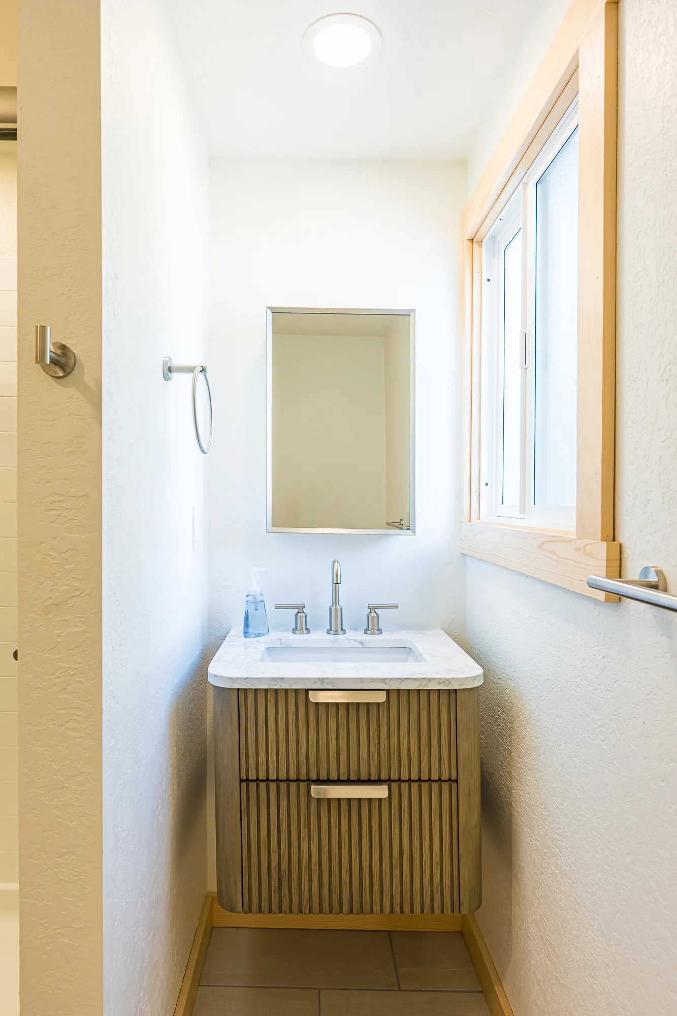 Narrow powder room with a wall-hung vanity and a window, remodeled by CKS Builders LLC