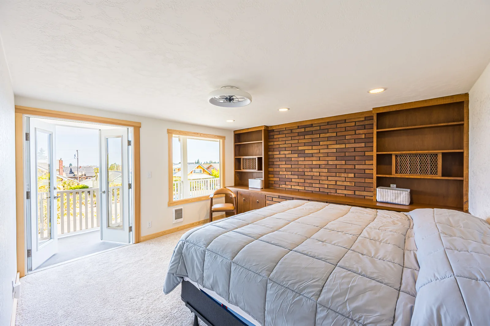 Primary bedroom with built-in shelving around a brick accent wall and French doors to a deck, remodeled by CKS Builders LLC