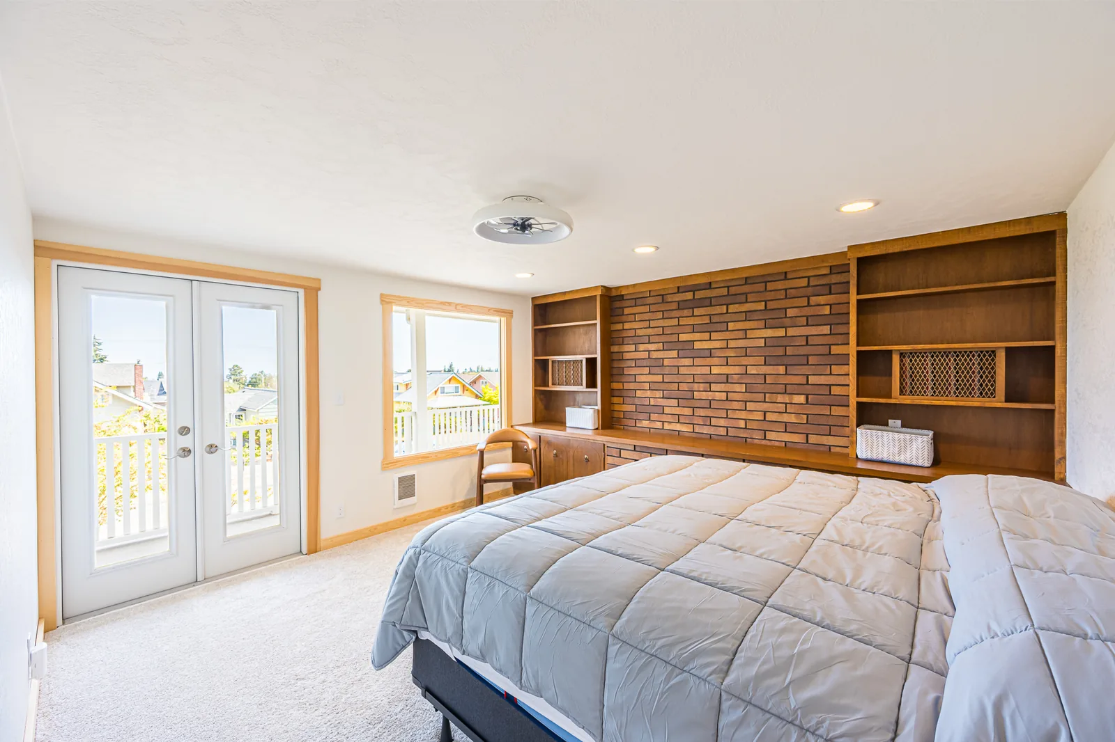 Primary bedroom with French doors to a deck and built-in shelves around a brick wall in a home remodeled by CKS Builders LLC