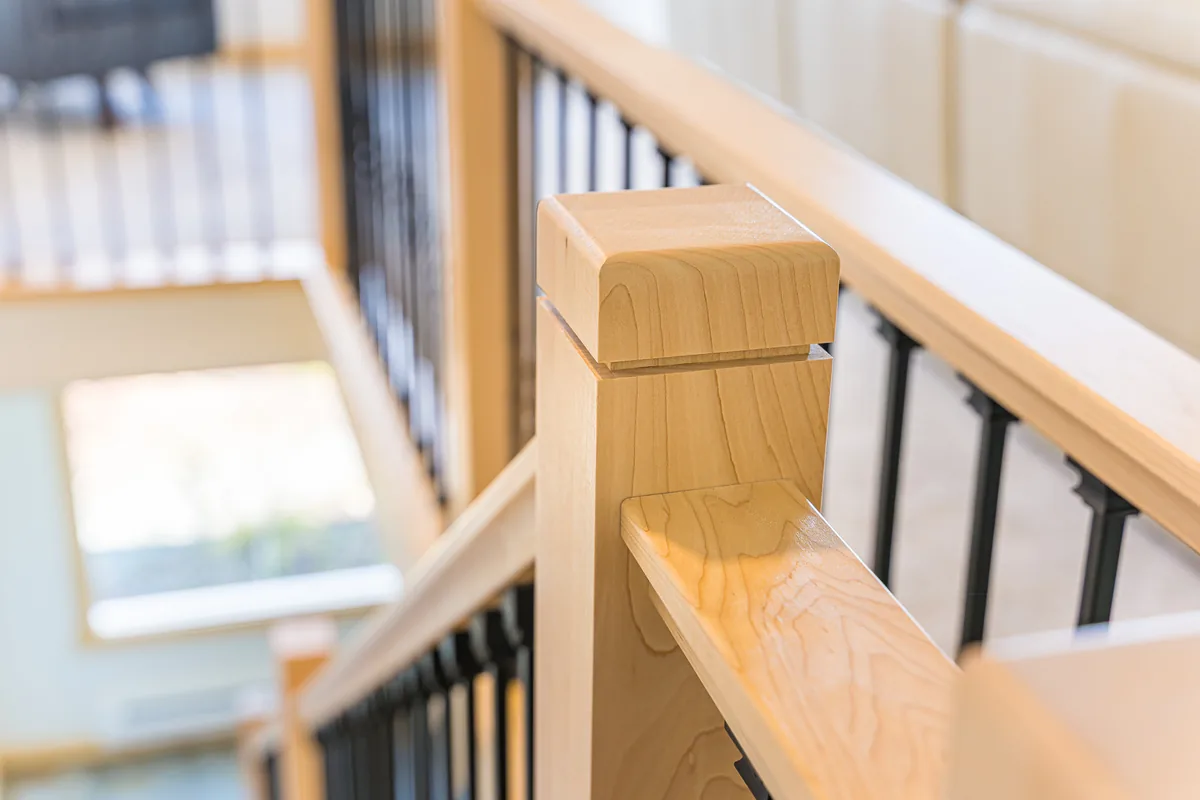 Close-up of a maple railing post and black metal balusters from a remodel by CKS Builders LLC