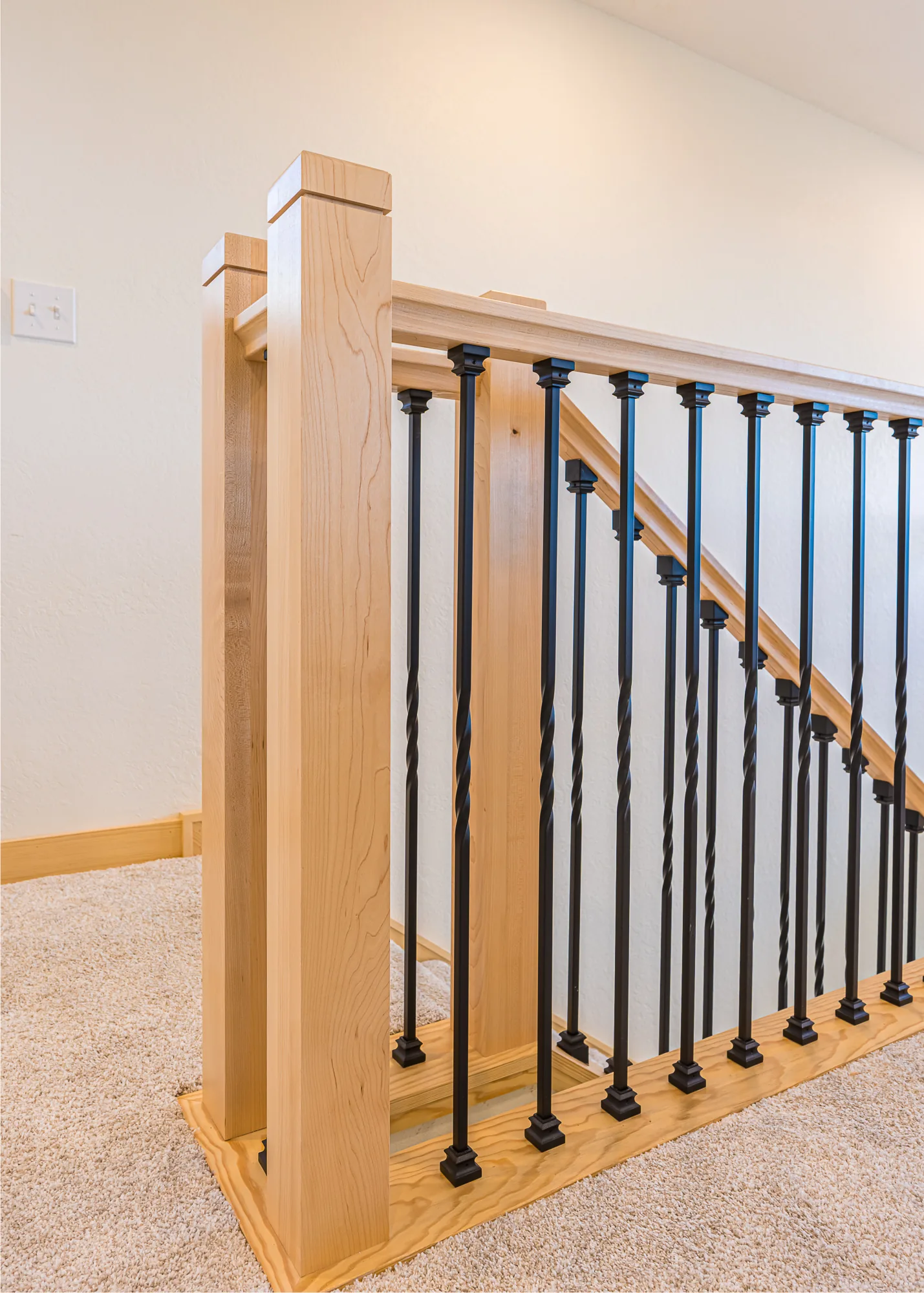 Maple newel post and black metal balusters at the top of a staircase in a home remodeled by CKS Builders LLC