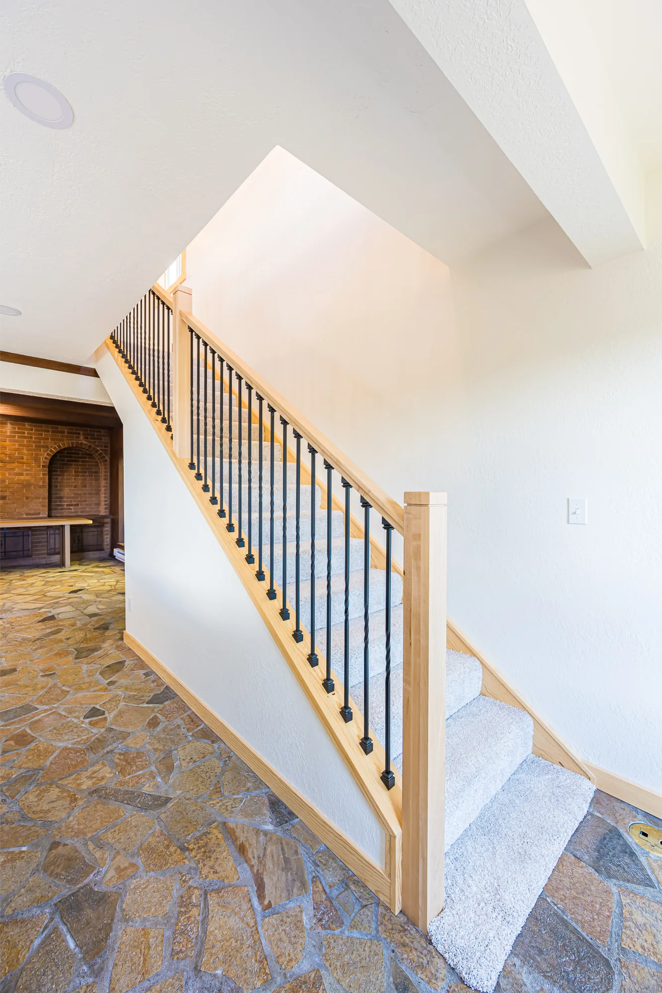 Carpeted staircase with a maple railing rising from a flagstone floor in a home remodeled by CKS Builders LLC