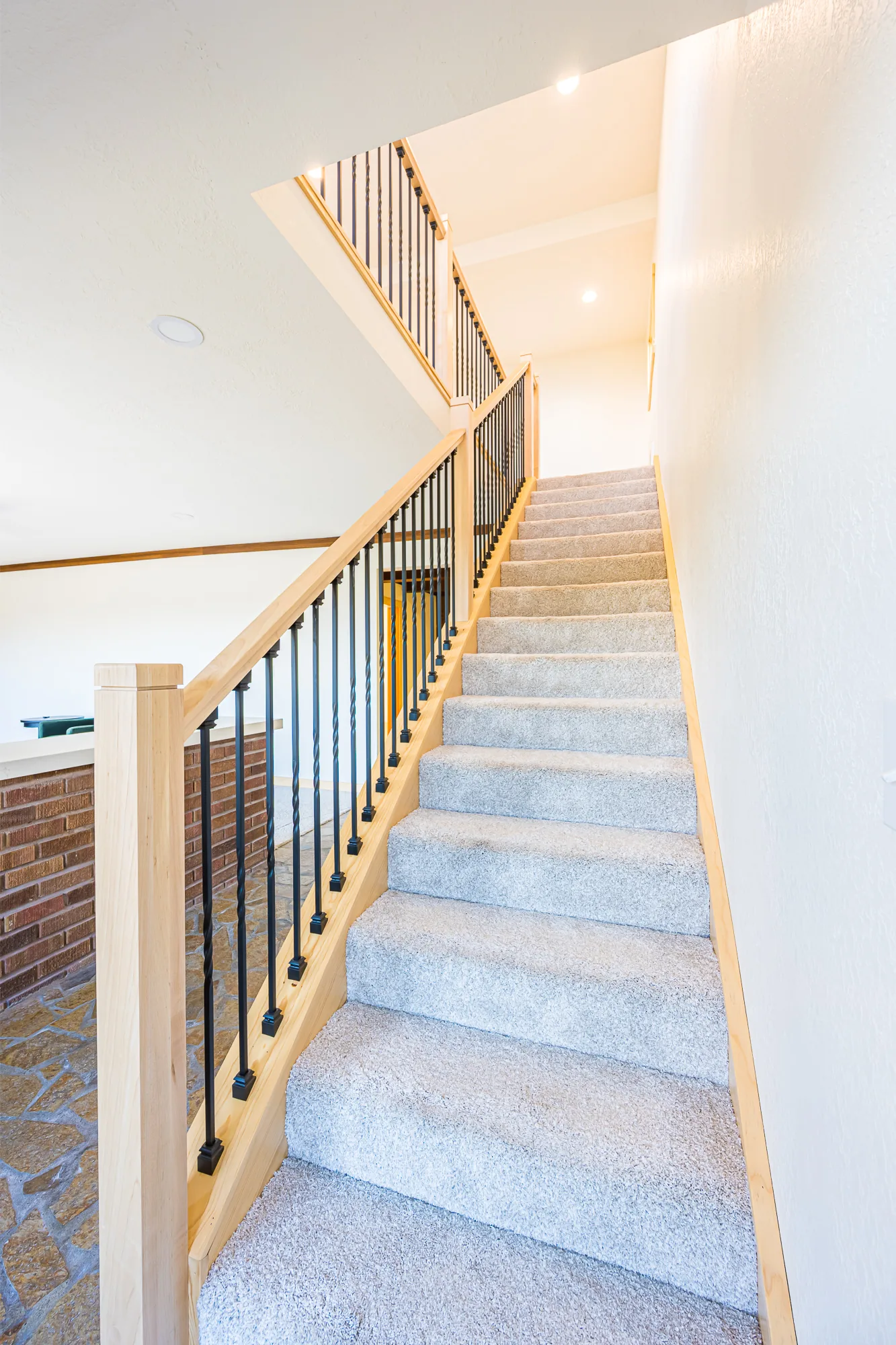 Carpeted staircase with a maple handrail and black metal balusters in a home remodeled by CKS Builders LLC