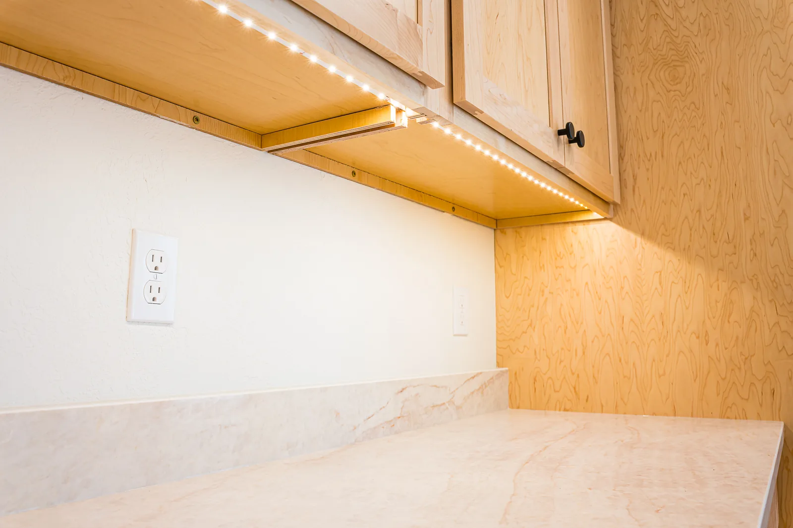Under-cabinet lighting above a light countertop beneath maple cabinets, remodeled by CKS Builders LLC