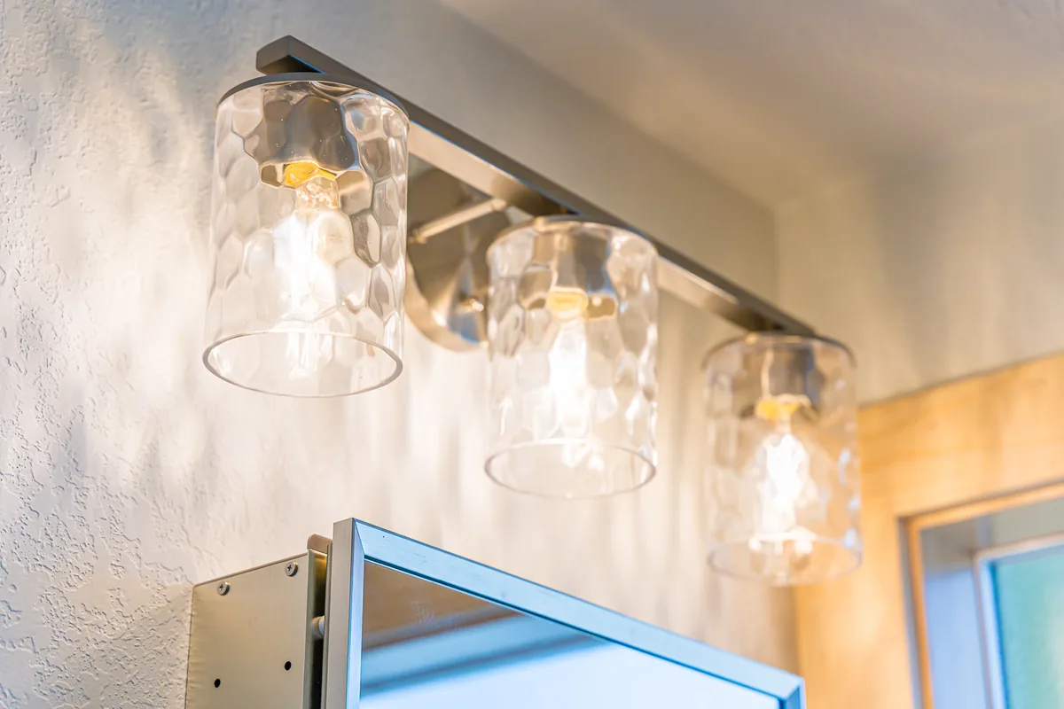 Three-light glass vanity fixture above a mirror in a bathroom remodeled by CKS Builders LLC