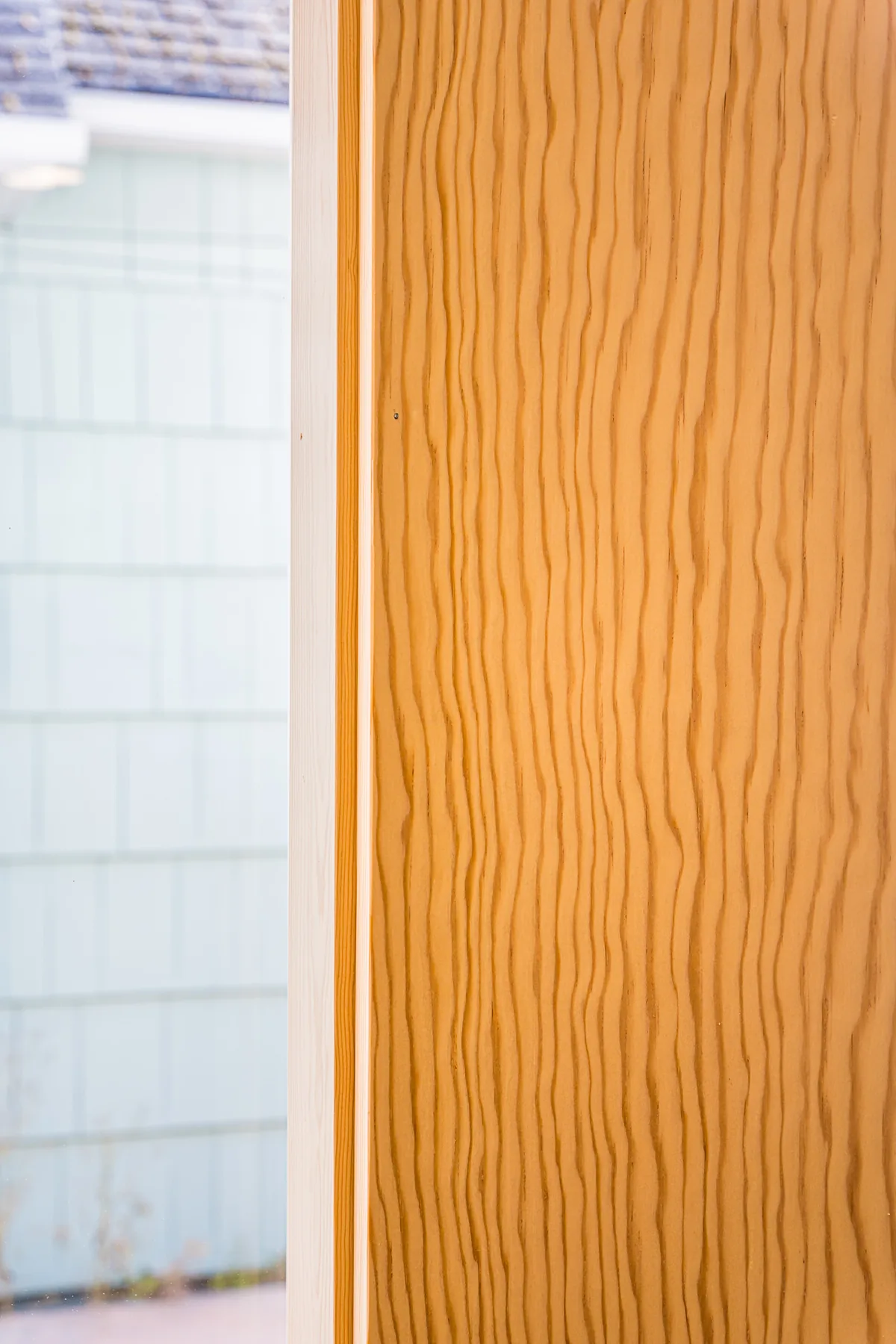 Close-up of vertical-grain wood window trim, with shingle siding visible through the glass, from a remodel by CKS Builders LLC